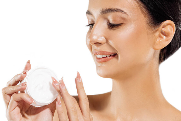 Woman's hands are about to apply face cream. Holding moisturizing lotion. Close-up of a young beautiful girl face applying a moisturizer, on a white background - Foto, imagen