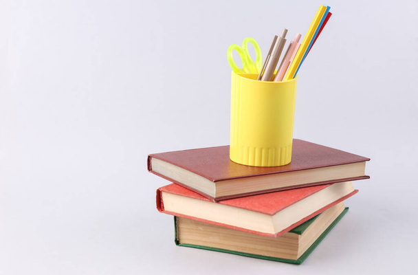 Schoolbenodigdheden in beker op een stapel boeken op een witte achtergrond - Foto, afbeelding