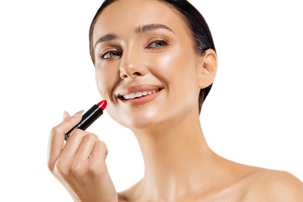 Portrait of girl coloring lips with bright red lipstick on a white background. Close-up photo of a focused girl applying lipstick at a beautician getting ready for a date and doing makeup - Φωτογραφία, εικόνα