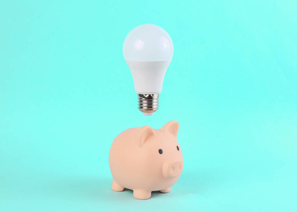 Piggy Bank With A Flying Light Bulb On A Blue Background. Minimal idea, inspiration concept - Фото, изображение