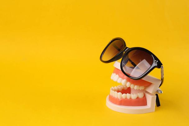 Minimal summer concept. Plastic model of a human jaw with sunglasses on yellow background - Photo, Image