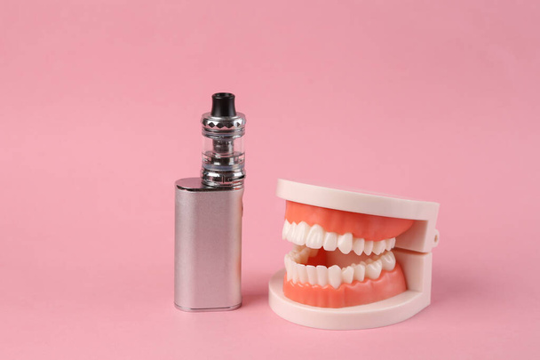 Модель челюсти и электронное ваппинговое устройство на розовом фоне. - Фото, изображение