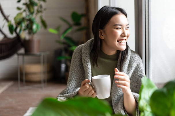 Happy asian woman drinking morning coffee and laughing, looking outsie window cheerful - Φωτογραφία, εικόνα