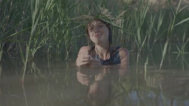 Beautiful water maiden with a wreath on her head, smiling comes out of the water - Footage, Video