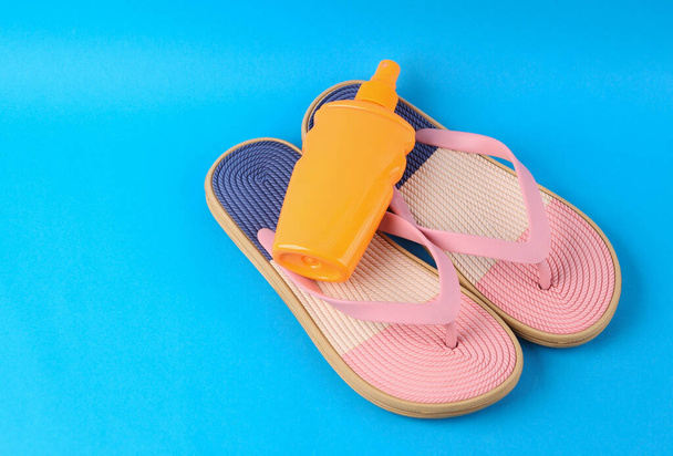Tongs colorées avec bouteille de crème solaire sur fond bleu. Concept vacances plage.  - Photo, image