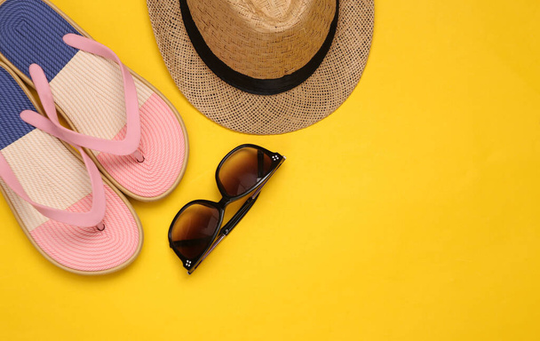 Straw hat with sunglasses and flip flops on yellow background. Top view. Copy space - 写真・画像