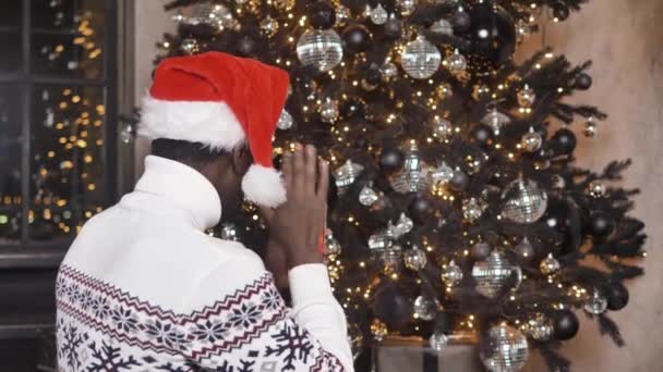 Afrikalı-Amerikalı bir adam kız arkadaşıyla bir Noel ağacının arka planında video bağlantısı kuruyor. - Video, Çekim