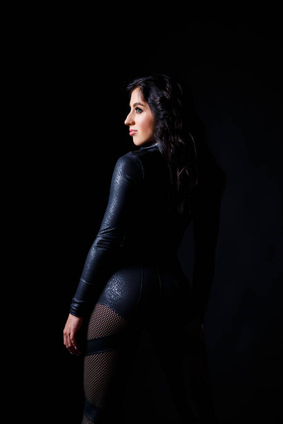 Young beautiful woman in black bodysuit posing in studio on black background - 写真・画像