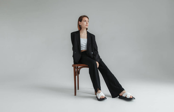 Fashion shot of young stylish woman in black suit sitting on a chair in the studio. Lifestyle - Фото, зображення