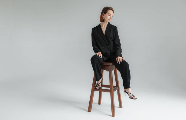 Szexi fiatal nő, kabátban, meztelen testen, nadrágban, aki a stúdióban ül a széken. Divatfotózás - Fotó, kép