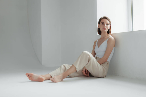Young stylish woman sitting by a light window in a white room - Photo, image