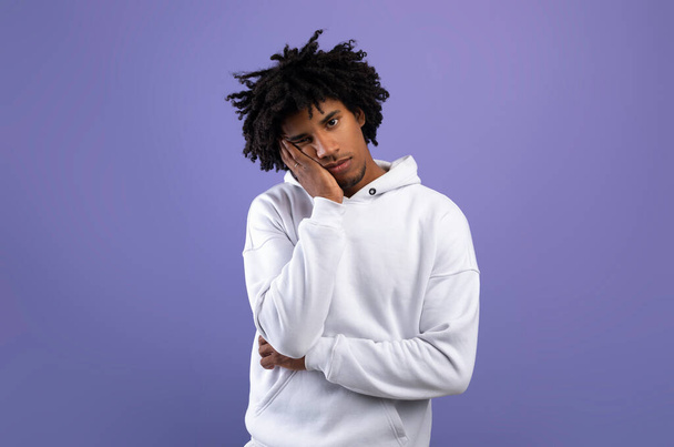 Portret van zwart tiener guy gevoel verveeld, leunend op zijn hand, het hebben van saaie dag op violette studio achtergrond - Foto, afbeelding