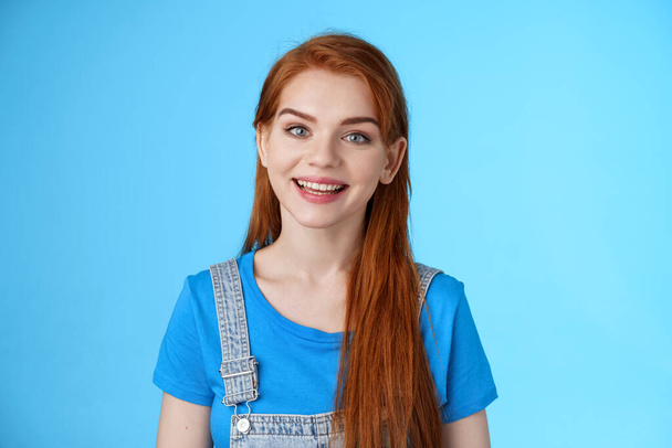 Friendly confident pleasant redhead woman helpfully look camera, smiling joyfully, have conversation customer, give advice, stand upbeat good positive mood blue background, grin amused - Photo, Image