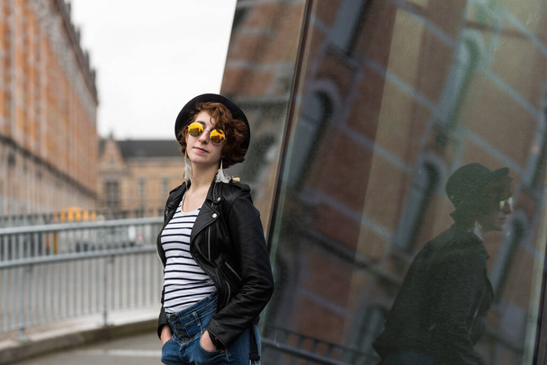 Relaxed portrait of a twenty year old girl wearing a hat and sunglasses with an urban background - Fotoğraf, Görsel