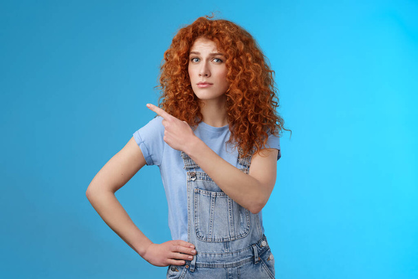Unsure silly timid hesitant cute redhead curly-haired ginger girl frowning uncertain asking your opinion questioned look camera pointing upper left corner confused worried blue background - Photo, Image