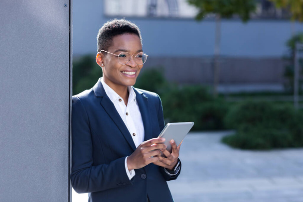 Молода афроамериканська бізнес-жінка біля офісу використовує планшетний комп'ютер, щаслива студентка посміхається і любить онлайн-навчання - Фото, зображення