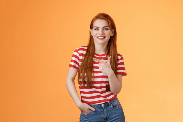 Carefree modern 20s female student chatting friends discuss left copy space, pointing left relaxed casual pose, smiling camera joyfully, introduce advertisement product, orange background - Photo, Image