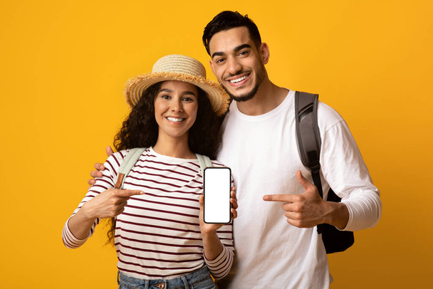 Alegre pareja de viajeros de Oriente Medio señalando a Smartphone con pantalla en blanco - Foto, Imagen