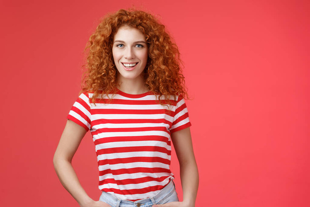 Sassy confident cheeky good-looking redhead curly-haired woman hold hands pockets smiling daring assertive motivated have perfect summer days wear striped trendy t-shirt stand red background - Photo, Image