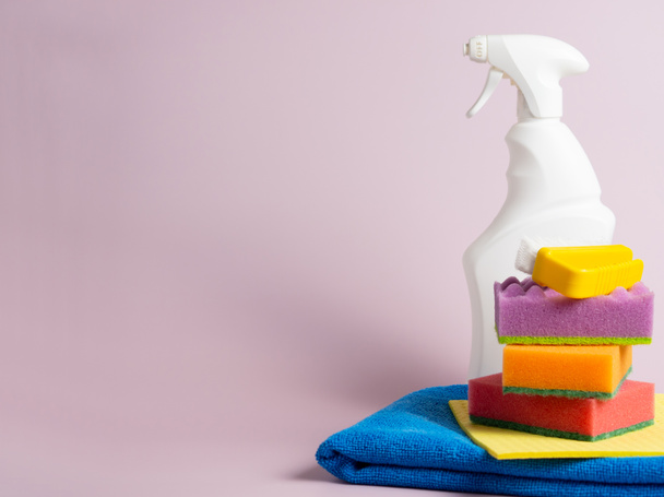Белая бутылка, тряпки, губка на фиолетовом фоне, Набор для мытья различных поверхностей на кухне, в ванной комнате и других помещениях. копировальное пространство - Фото, изображение