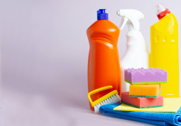Reinigungsprodukte für zu Hause auf lila Hintergrund Kopierraum. Reinigung und allgemeine Reinigungskonzept. Waschmittelflaschen, Pinsel, Schwamm und Lumpen - Foto, Bild