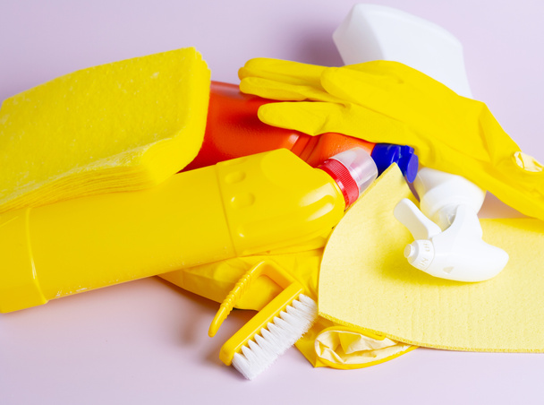 Stapel von Waschmittelflaschen, mehrfarbigen Tüchern, Schwämmen und Handschuhen auf isoliertem lila Hintergrund mit Copyspace - Foto, Bild