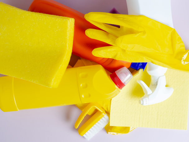 Stapel von Waschmittelflaschen, mehrfarbigen Tüchern, Schwämmen und Handschuhen auf isoliertem lila Hintergrund mit Copyspace - Foto, Bild
