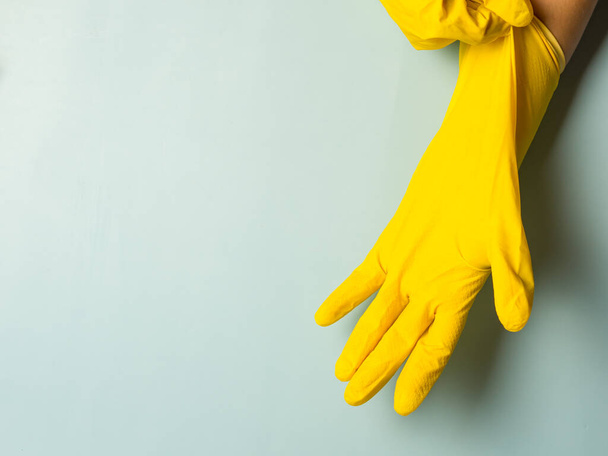 Ev hanımı sarı lateks temizleme eldivenlerini giyip mavi arka planda fotokopi alanı kullanıyor. - Fotoğraf, Görsel