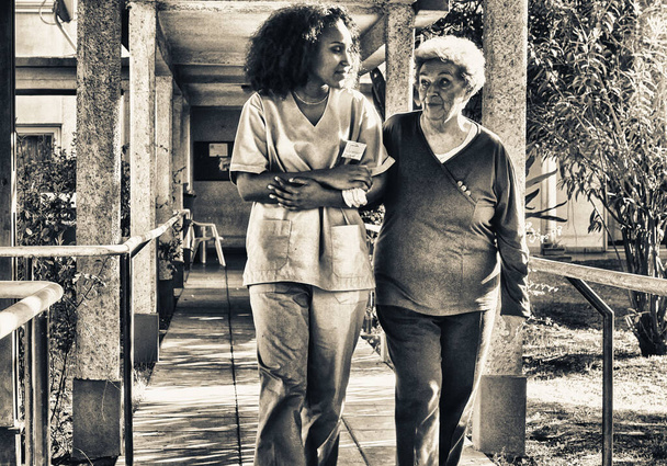 Afrykanka rozmawia ze starszą emerytką na podwórku szpitala. Koncepcja szczęścia i emerytury. - Zdjęcie, obraz