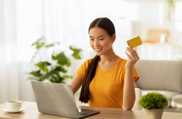 Проста онлайн концепція безконтактних платежів. Захоплена азіатська жінка робить покупки на ноутбуці та використовує кредитну картку
 - Фото, зображення