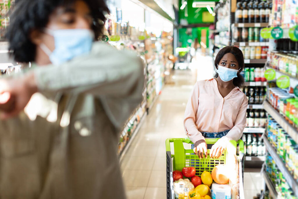 Mujer negra asustada mirando a un tipo enfermo tosiendo en el supermercado - Foto, Imagen