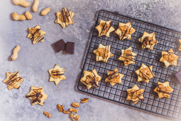 Biscoitos caseiros em forma de estrela com cobertura de caramelo de noz e chocolate, em um rack de refrigeração e fundo cinza, vista superior - Foto, Imagem