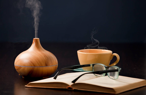 Relaxation at home with aromatherapy oil diffuser, yellow tea cup, book, reading glasses. Aroma essence of health, wellness aromatherapy home aromatic tranquil therapy. - Photo, Image