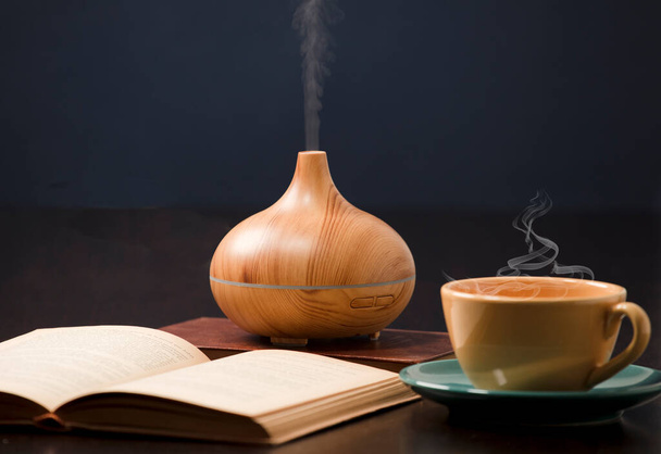 Ontspanning thuis met aromatherapie olie diffuser, gele thee kopje, open boek. Aroma essentie van gezondheid, wellness aromatherapie thuis aromatische rustige therapie. - Foto, afbeelding