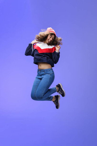 Girl jumping from happiness and delight feeling carefree close eyes and smiling broadly enjoying moment having fun raising hands being dreamy and playful over blue background - Photo, Image
