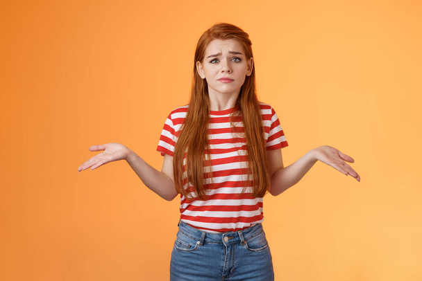 Uneasy questioned and clueless lovely modern stylish redhead woman shrugging spread hands sideways unaware, grimacing perplexed, tough question, have no answer, stand orange background - Valokuva, kuva
