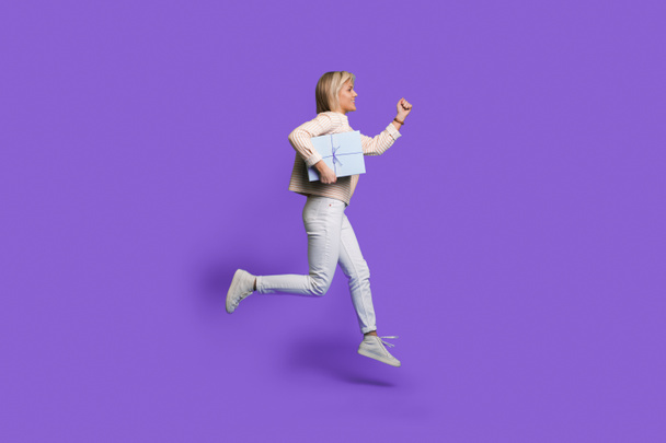 Повна фотографія профілю тіла бічної жінки, що стрибає вгору, тримає подарунок коробки, працює, ізольовано на фіолетовому кольоровому фоні
 - Фото, зображення
