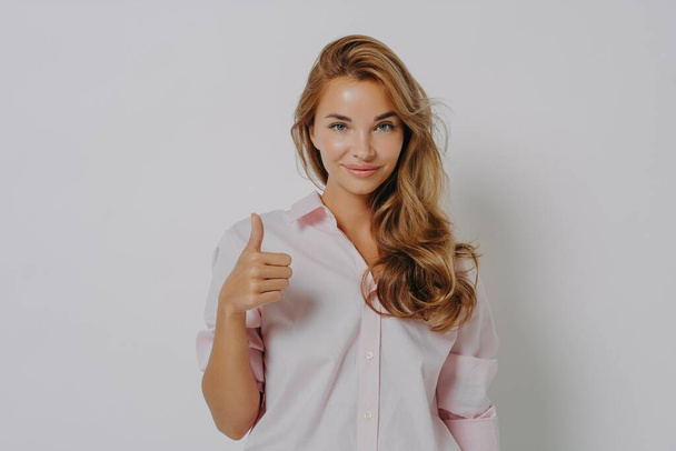 Enthusiastic young Caucasian woman keeps thumb up recommends something very good says yes - Photo, Image