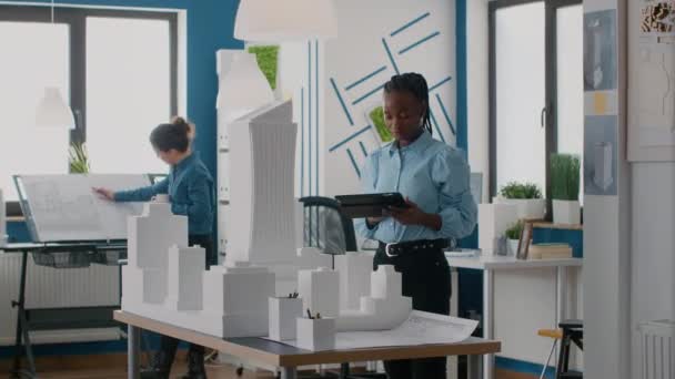 Építész digitális táblagéppel tervezni elrendezés épület modell és makett az irodában - Felvétel, videó