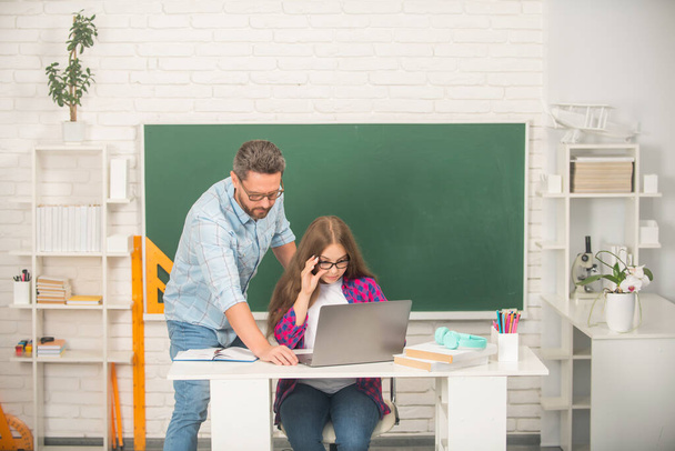 curious father and child study at school with laptop on blackboard background, back to school - Foto, Imagen