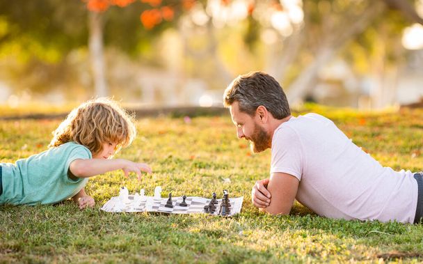 šťastná rodina otce a syna dítě hrát šachy na zelené trávě v parku venkovní, otcové den - Fotografie, Obrázek