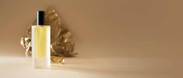 Frasco de perfume e papel dourado desintegrado em fundo bege formato banner horizontal com espaço de cópia - Foto, Imagem