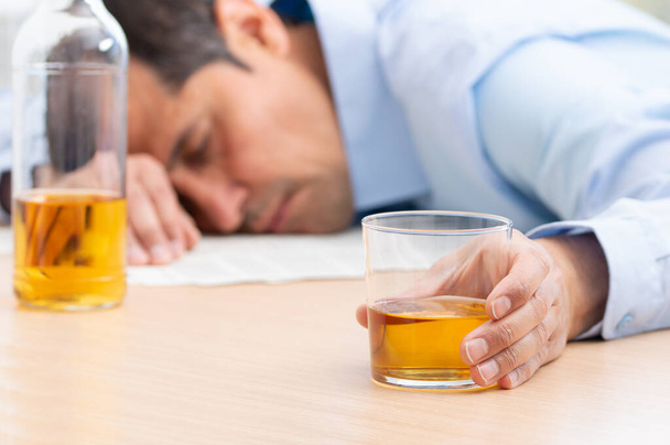 Close up of stressed businessman holding a glass of whiskey he sleeping and Data Charts,business document at office desk. alcohol addiction and drunk businessman concept - Foto, imagen