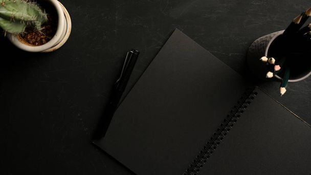 Mínimo espacio de trabajo oscuro con páginas en blanco negro en cuaderno con papelería sobre la mesa. vista superior - Foto, Imagen