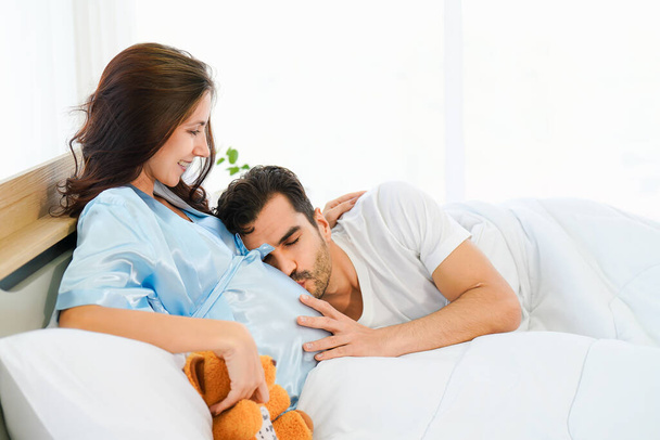 portrait of happy pregnant wife and husband lying together on bed in bed room at home - Photo, image