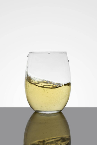 crystal glass with moving white wine making waves and white background - Photo, Image