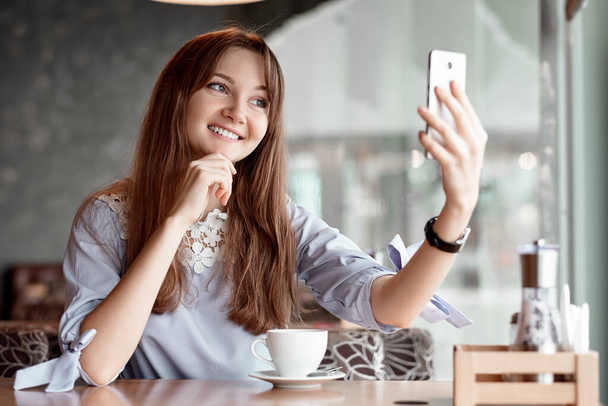 Young business woman using her smart phone and smiling in coffee shop. - Фото, изображение
