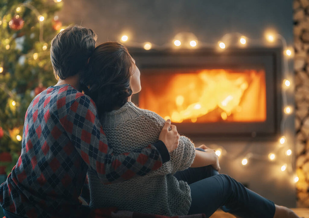 Loving couple relaxing near fireplace Christmas tree at home. - Foto, afbeelding