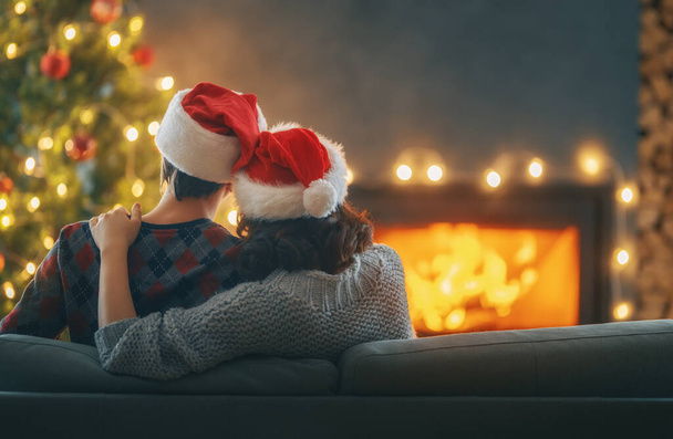 Loving couple relaxing near fireplace Christmas tree at home. - Фото, изображение