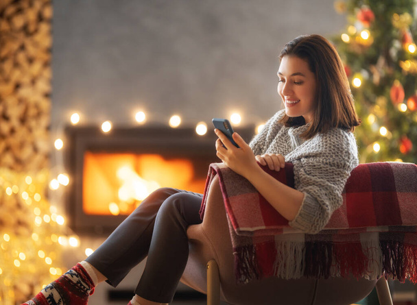 Woman is using mobile phone sitting near Christmas tree. - Foto, imagen